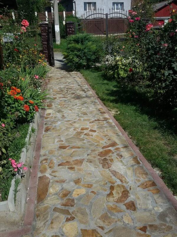 Alee de grădină din piatră rustică naturală într-o curte rezidențială cu flori și gazon