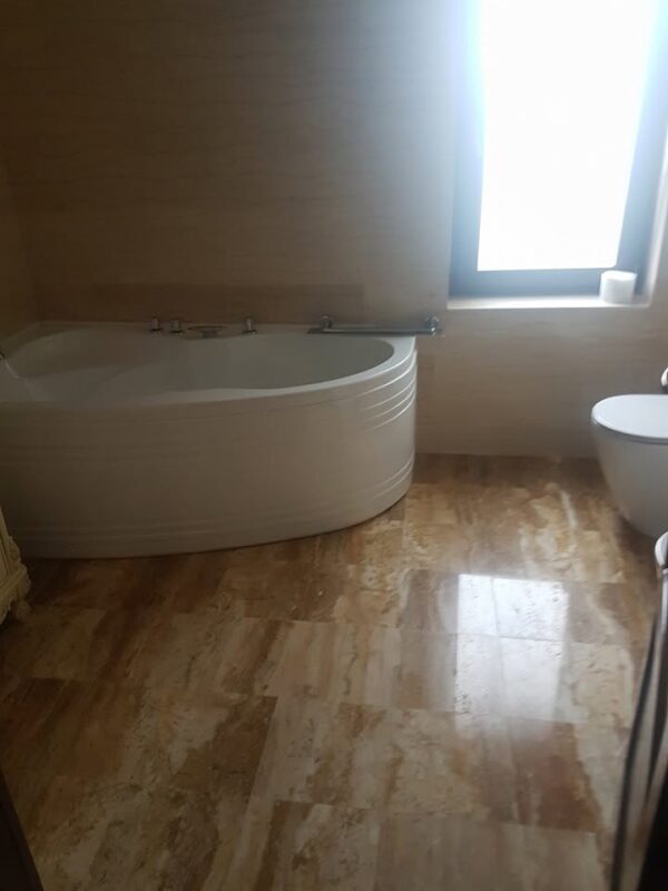Baie modernă cu pardoseală din travertin natural și cadă de colț albă